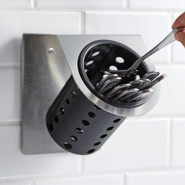 A hand holding a spoon in a Steril-Sil stainless steel flatware organizer with a black plastic cylinder.