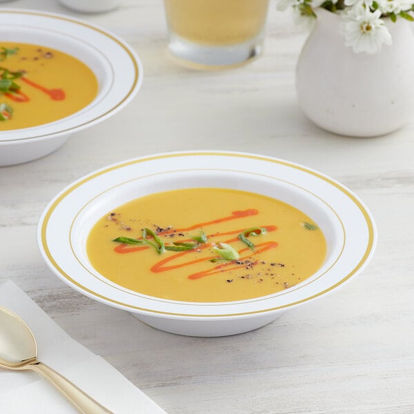 Two Visions white plastic bowls of soup with gold bands and garnish on a table.