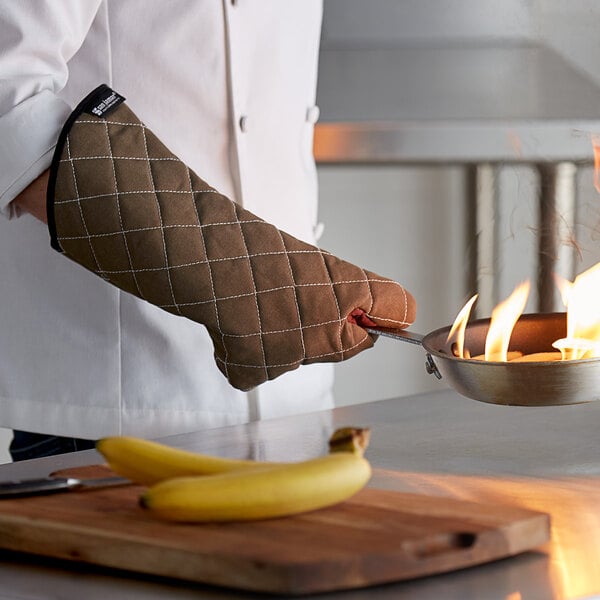 A person wearing San Jamar Bestguard oven mitts holding a pan with flames.