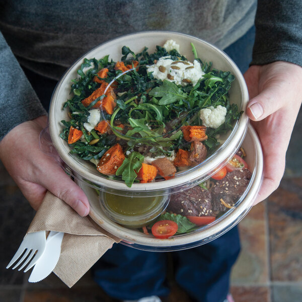A clear, flat compostable plastic lid designed to fit 24-46 oz. coupe bowls, shown covering two salad bowls.