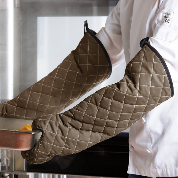 A person wearing San Jamar Bestguard oven mitts holding a tray of food.