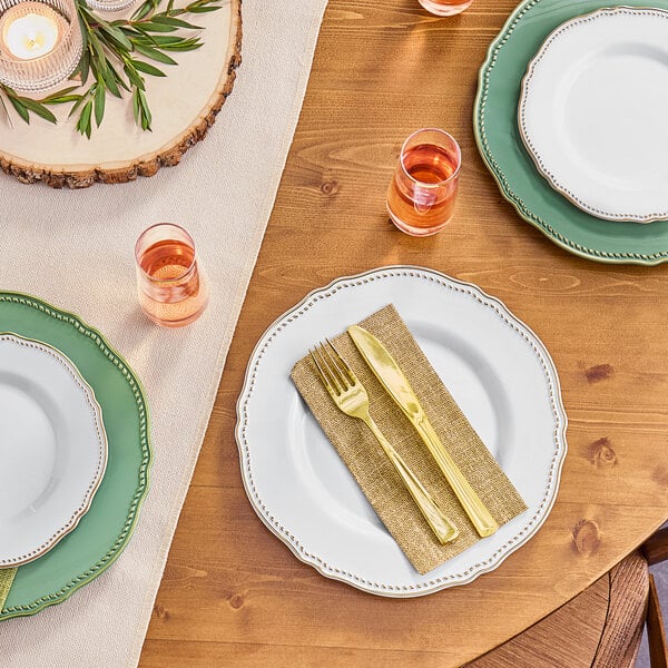 A table setting with a white plate, gold trim, and a fork and knife on a burlap print dinner napkin.