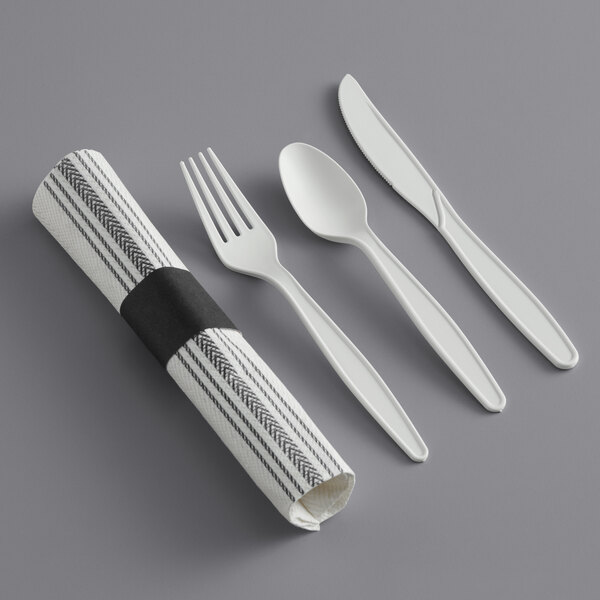 A white napkin roll with black and white striped print containing a fork, spoon, and knife with white handles.