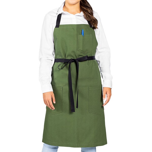 A woman wearing a sea green Uncommon Chef Aura bib apron with black webbing.