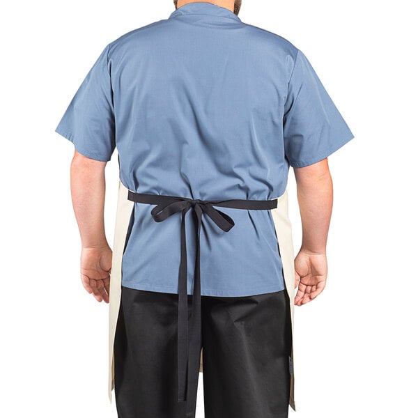 A man wearing an ivory Uncommon Chef bib apron with black webbing over a blue shirt and black pants.