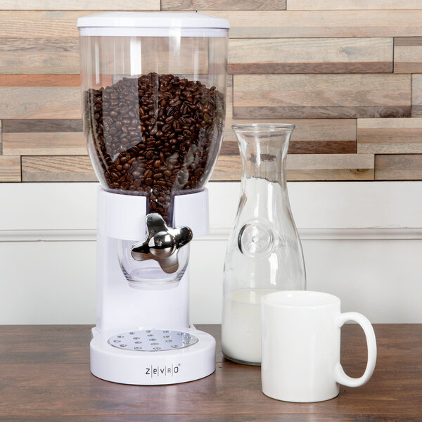 A white Zevro dry food dispenser on a table next to a glass of milk.