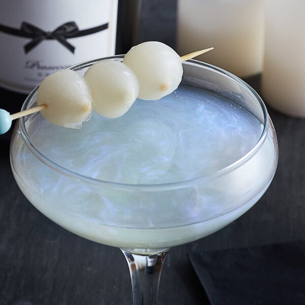 A cocktail with blue shimmer on a stick over a white drink.