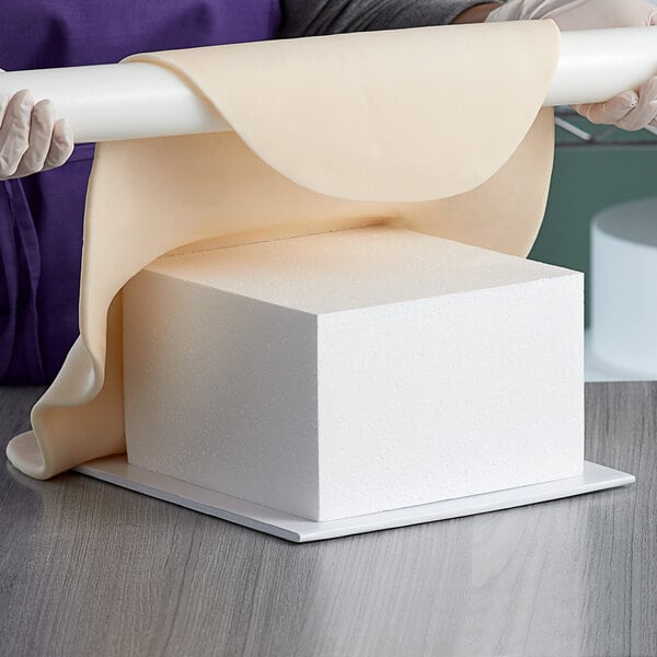 A person holding a Baker's Mark foam square cake dummy over a white table.