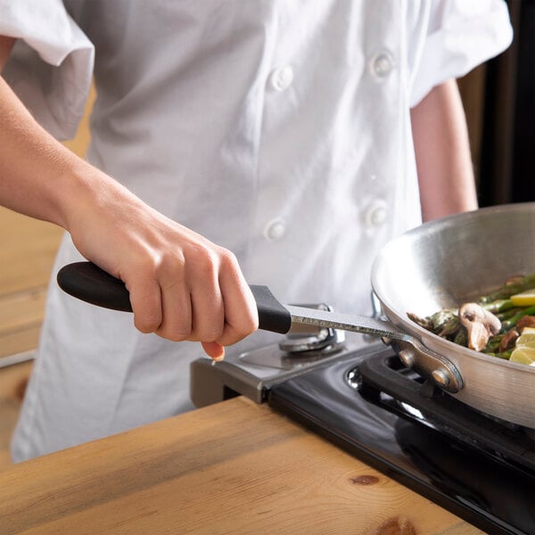 A hand using a San Jamar black silicone handle holder to cook food in a pan.