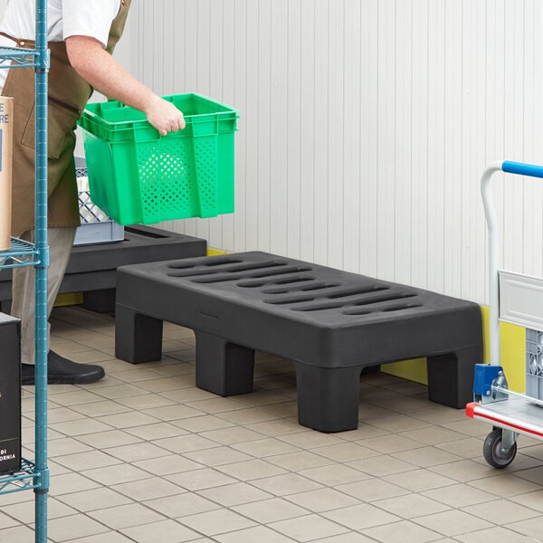 A man carrying a green Regency Dunnage Rack in a warehouse.