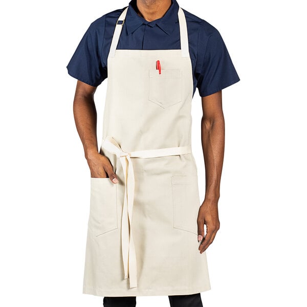 A man wearing a sand beige Uncommon Chef apron with natural webbing and red pockets.
