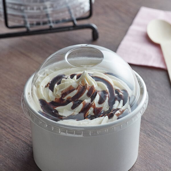 A clear dome lid on a cup of ice cream with chocolate sauce.