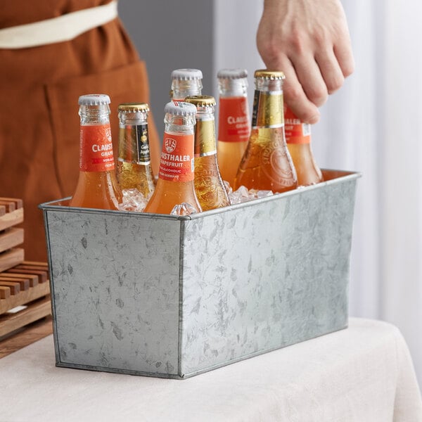 A person holding a metal rectangular beverage tub with bottles of beer inside.