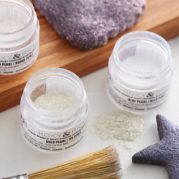 A close-up of a jar of Roxy & Rich Super Pearl Sparkle Dust with white and green powder, a star, and a brush.