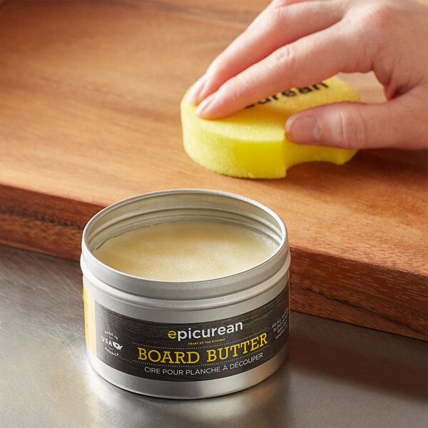 A hand using a yellow sponge to clean Epicurean board butter.