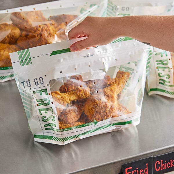 A person's arm holding a "To Go Fresh" fried chicken bag.