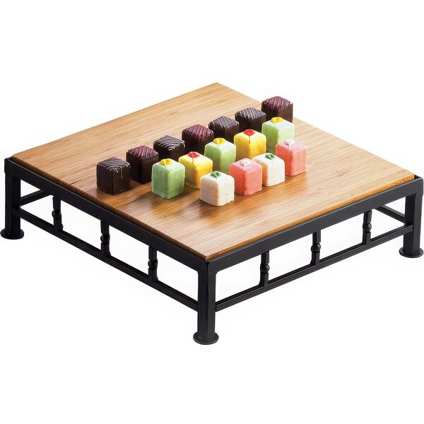 A Cal-Mil square black iron riser with bamboo top holding colorful square candies on a wood table.