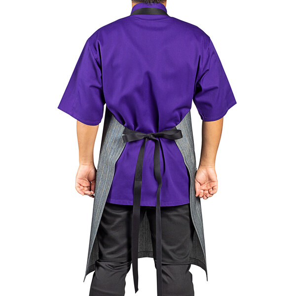 A man wearing a purple shirt and a black denim Uncommon Chef Renegade bib apron.