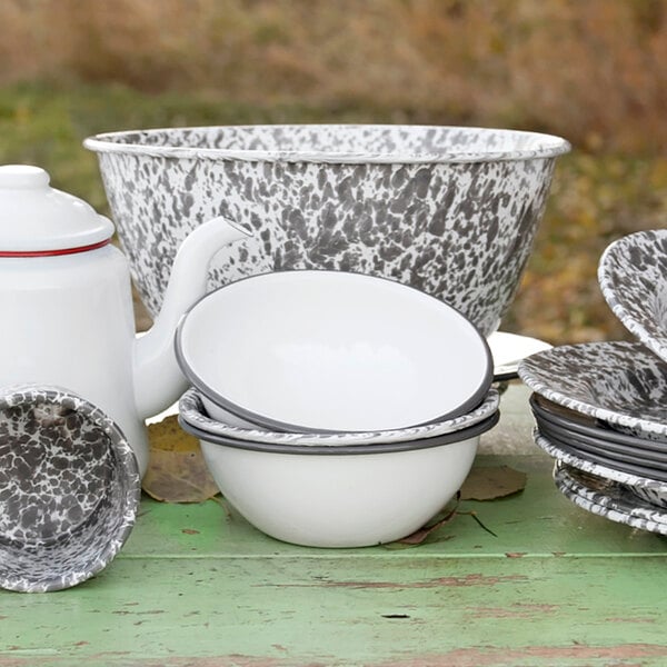 A close-up of a Crow Canyon Home white enamelware bowl with a grey rim on a table with a teapot and dishes.