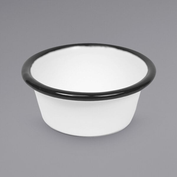 A close up of a white Crow Canyon Home enameled ramekin with a black rim.