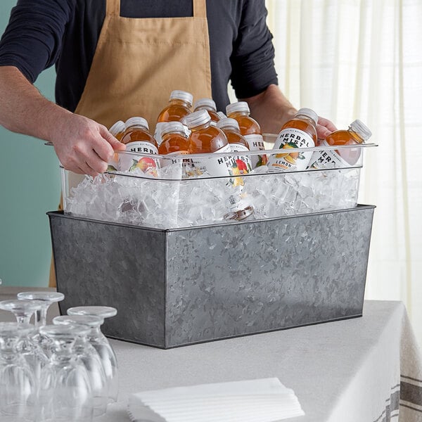 A man holding a American Metalcraft beverage tub filled with bottles of liquid.