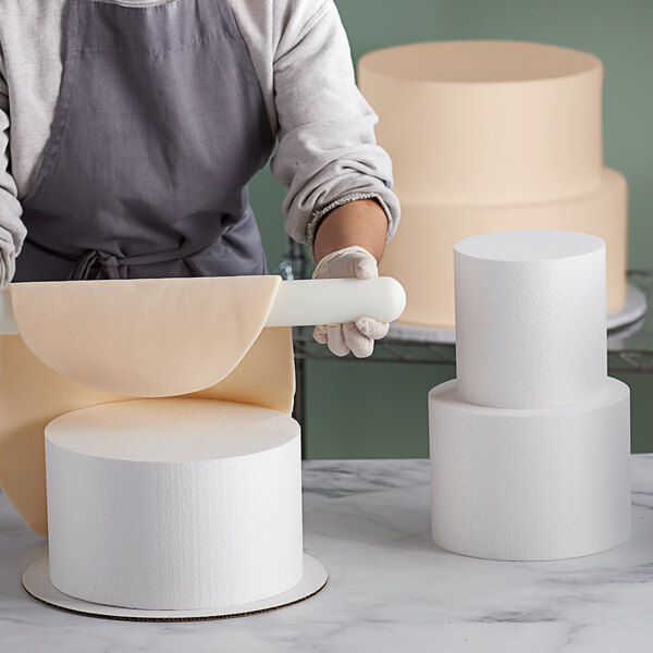 A woman using a rolling pin to make a cake over round white cake dummies.