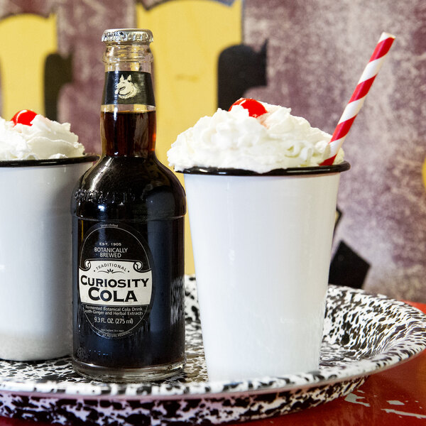 A white Crow Canyon Home enamel tumbler filled with dark liquid and whipped cream on a tray.