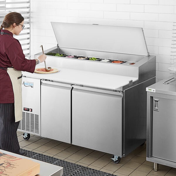 A woman in a red apron preparing food in an Avantco refrigerated pizza prep table.