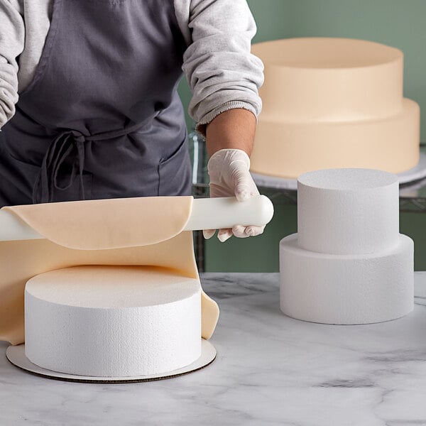 A person using a rolling pin to make a cake dummy.