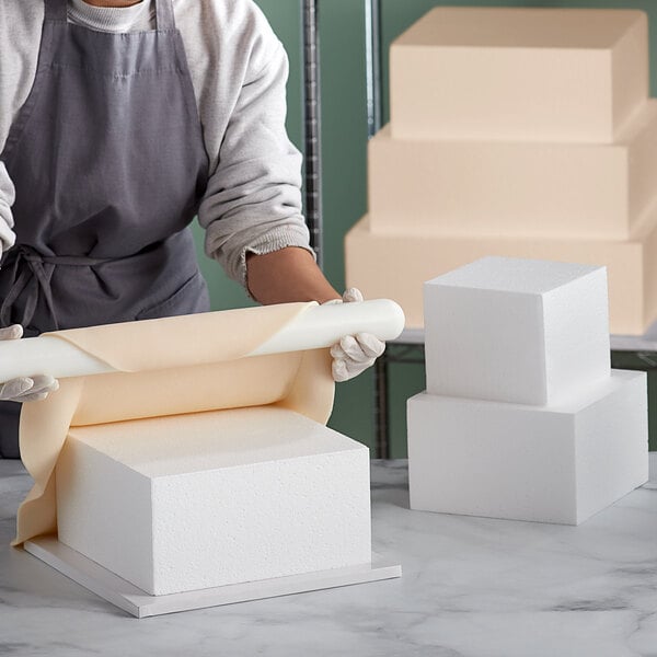 A woman cutting a foam cake dummy with a knife.