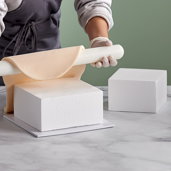 A person using a Baker's Mark square cake dummy to roll out dough.