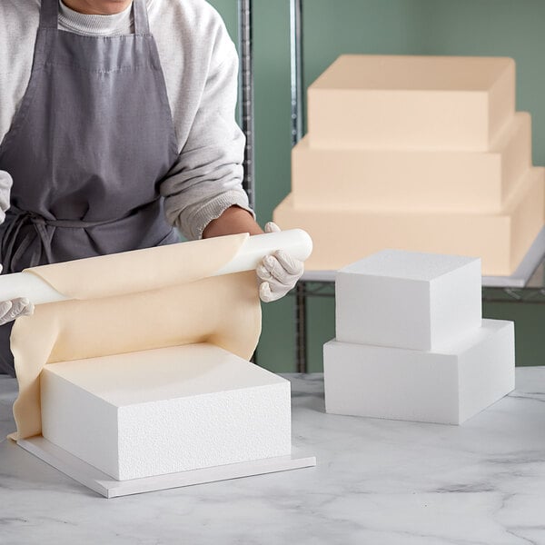 A person rolling out a Baker's Mark foam square cake dummy.