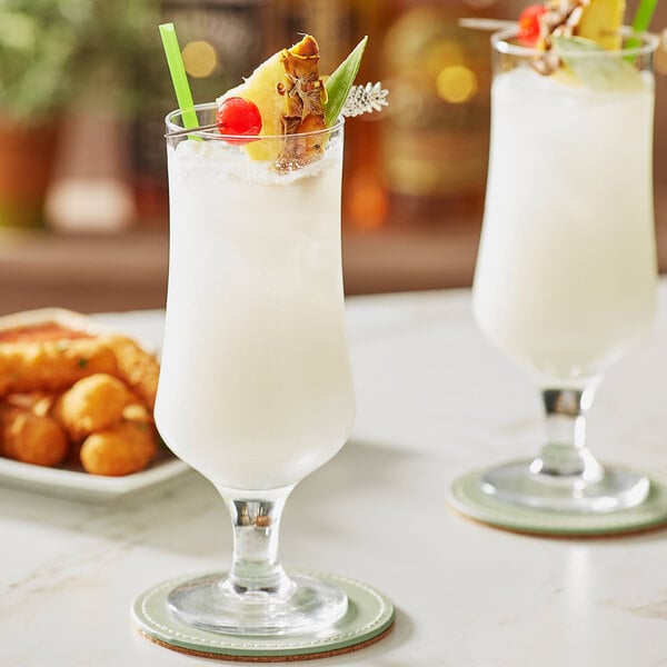 Two Acopa Select stemmed beer glasses with white liquid and pineapple garnish.