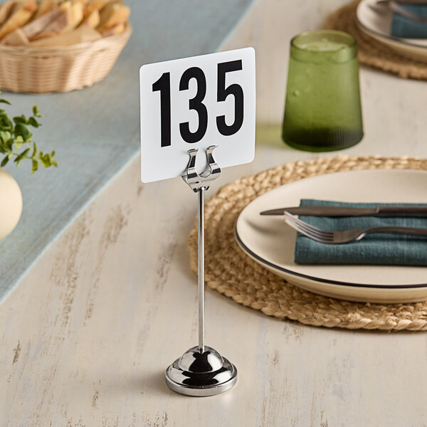 An American Metalcraft stainless steel harp table card holder with a number plate on a table.