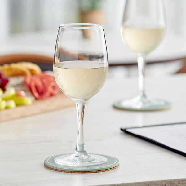 Two Acopa Select Flora wine glasses filled with white wine on a table.
