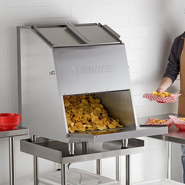 A man in an apron using a ServIt nacho chip warmer to fill a red bowl with chips.