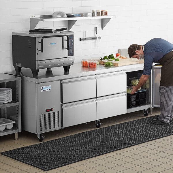 A man putting food into an Avantco undercounter refrigerator with drawers.