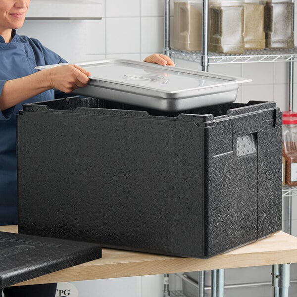 A woman in a professional kitchen using a Cambro black top-loading food pan carrier.