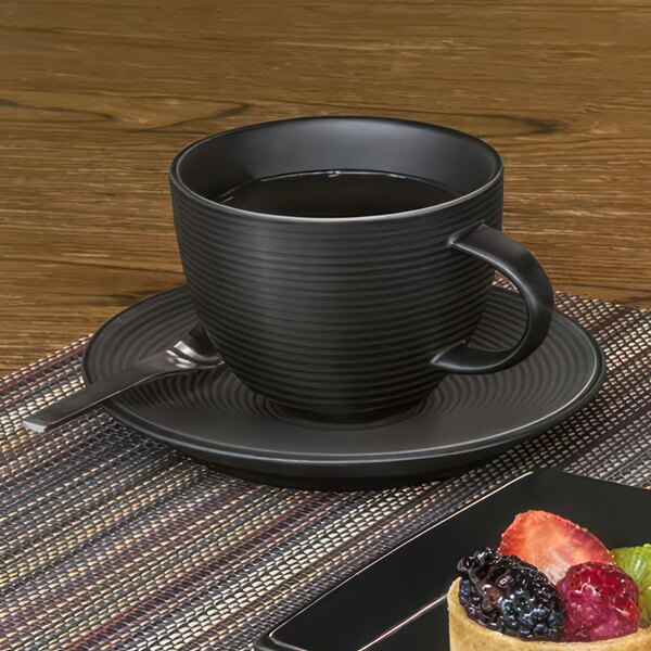 A Front of the House semi-matte black porcelain saucer with a cup of tea and a plate of fruit.