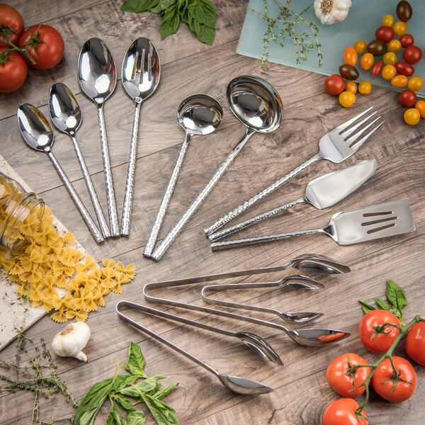 A Carlisle Terra stainless steel serving fork on a wood surface with other silverware.