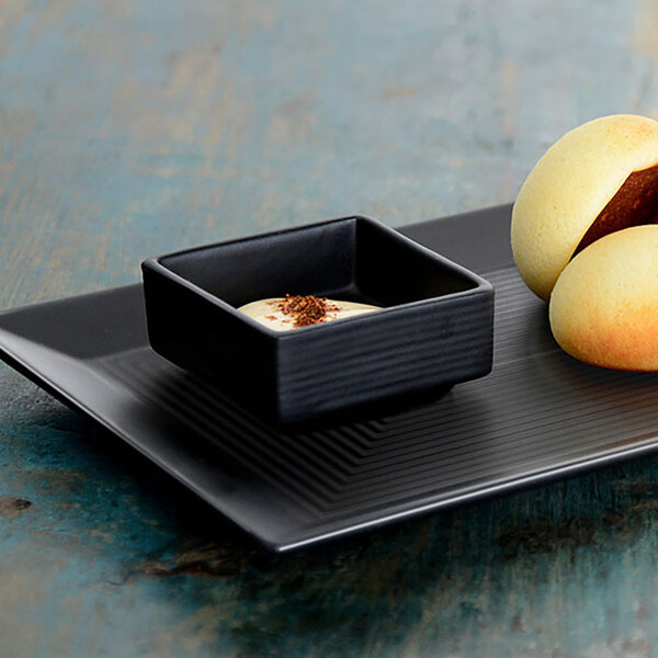 A black square Front of the House porcelain bowl with white sauce on a plate of food.