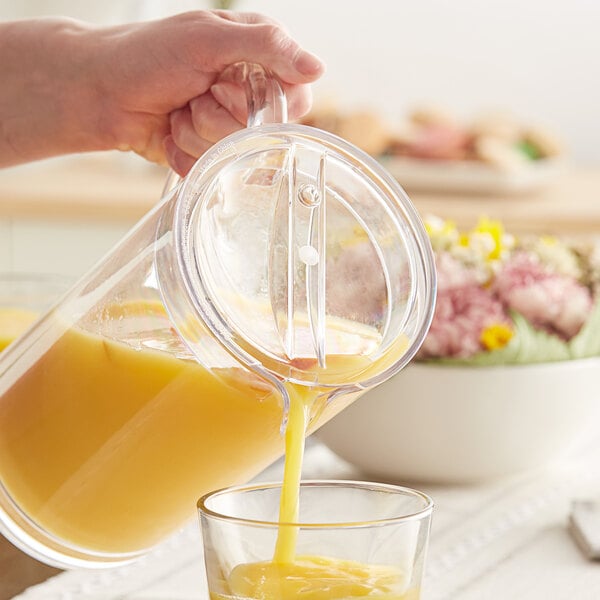 A person using a Carlisle Elan pitcher lid to pour orange juice into a glass.