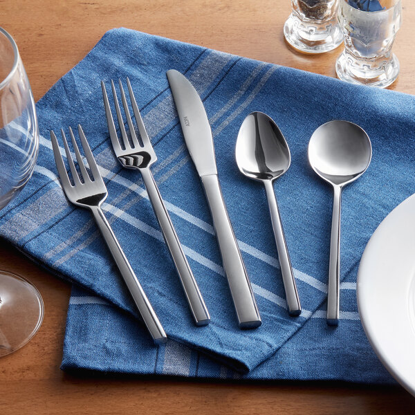 Acopa Phoenix stainless steel bouillon spoon on a blue cloth with silverware.