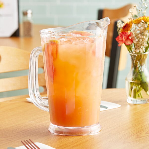 A clear plastic pitcher of orange juice on a table.