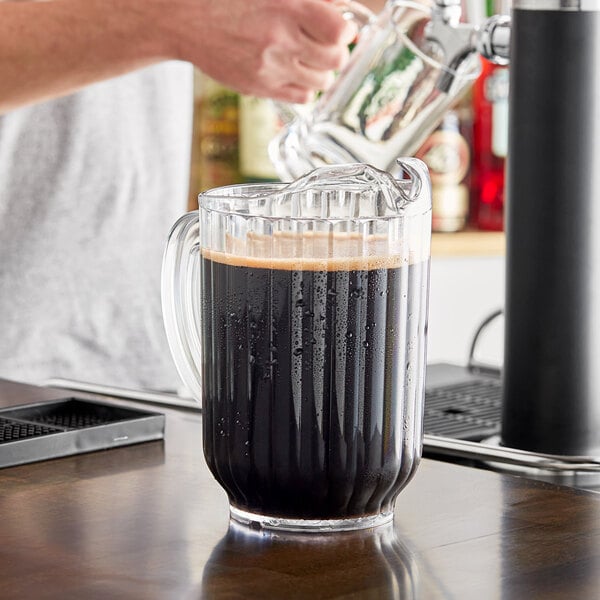 A person pouring dark liquid into a clear GET pitcher.