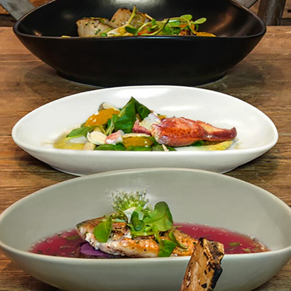 A group of Front of the House Tides oval porcelain plates with food on a table.