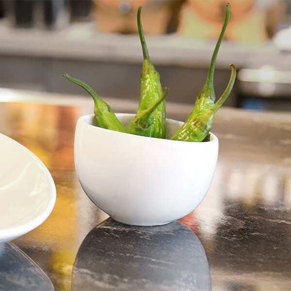 A white bowl filled with green peppers on a table.