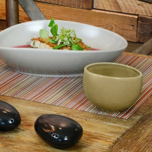 A close-up of a Front of the House Tides sea grass bowl filled with food on a table.