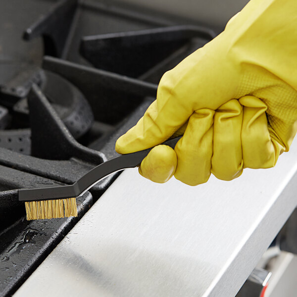 A person in yellow gloves using a Carlisle utility brush to clean a stove.