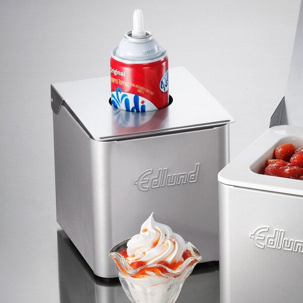 A stainless steel Edlund cold food pan with a black lid and a lid hole holding a glass dish of ice cream with white and orange toppings.